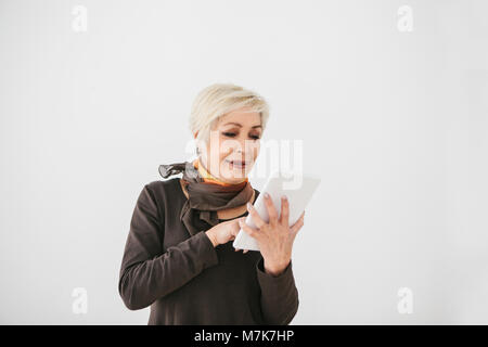 A positive modern elderly woman holds a tablet in her hands and uses it. The older generation and modern technology. Stock Photo