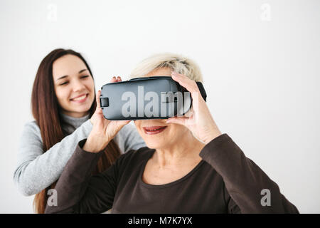 A young girl explains to an elderly woman how to use virtual reality glasses. The older generation and new technologies. Stock Photo