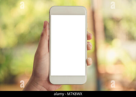 Mockup image of a hand holding and showing white smart phone with blank desktop screen in outdoor with blur green nature background Stock Photo