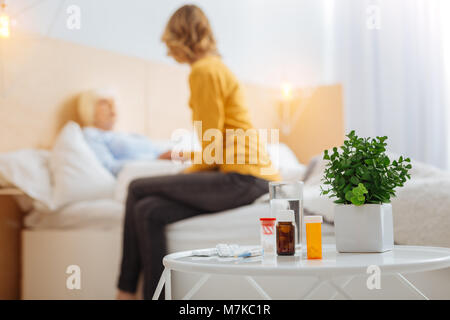 Necessary pills being on the table while an aged woman being in her bed Stock Photo