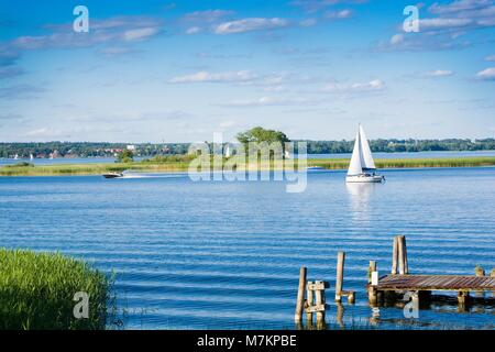 Empty wooden jetty on the lake shore with island and yachts in the background Stock Photo