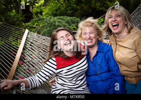 Three generations of women sitting in a hammock enjoying each others company. Stock Photo