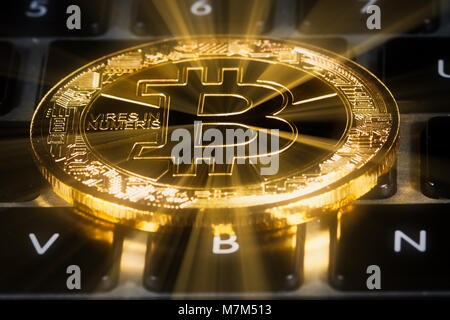 Bitcoin positioned on top of keyboard. Physical coin used to illustrate cryptocurrency and blockchain technology. Stock Photo