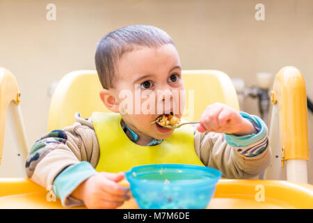 The boy 2 years eats porridge. Children's table. The concept of the child's independence. Stock Photo