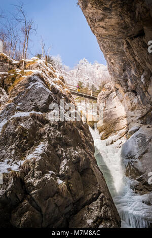 Young women standing on bridge high over the big frozen icy waterfall in snow covered gorge Baerenschuetzklamm in winter Stock Photo