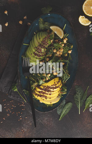 Healthy vegan avocado, chickpeas, kale salad in a vintage blue plate on a dark rusty background. Vegan food concept. Stock Photo