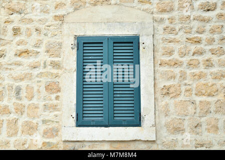 Window shut with wooden blinds of a coastal stone house Stock Photo