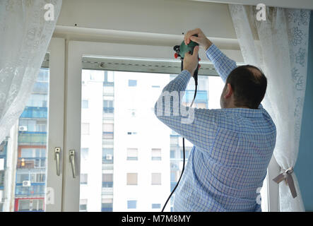 Man drilling a hole in a window frame in order to install a blind Stock Photo