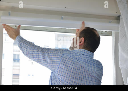 Man installing a new white blind on a window Stock Photo