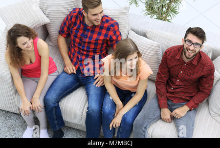 triumphant group of friends laughing while sitting on the couch in the living room Stock Photo