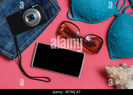 Smartphone, Swimsuit, Jeans, Sunglasses, Photo Camera, Seashell on Pink Background. Top View Travel Concept Mock up. Stock Photo