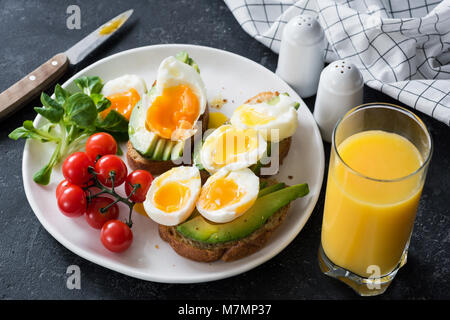 Avocado and poached egg toasts, salad and orange juice on stone table. Closeup view Stock Photo