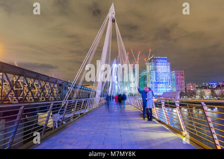 London, United Kingdom, February 17, 2018: long exposure of people walking and taking photos on Queen's Golden Jubilee Footbridges near Charring Cross station Stock Photo