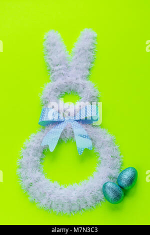 Easter holiday decorations on solid bright green background. Minimalist Easter decor. Easter bunny with sparkly eggs. Stock Photo