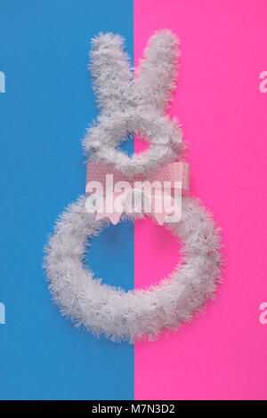 Easter holiday decorations on bright colors. White wire bunny on pink and blue background with polka dot bow tie. Stock Photo