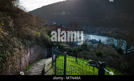 Beautiful view from the hill at the cityscape and river. Scenic stone road leading down. Sun rays are falling on the land and grass. Sunny day Stock Photo