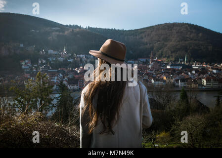 Young unrecognizable woman standing back on hill and looking on the cityscape. Trendy traveler in early morning exploring park with beautiful view Stock Photo