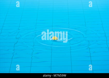 Tennis ball in the center of twirling water surface of a swimming pool. Stock Photo