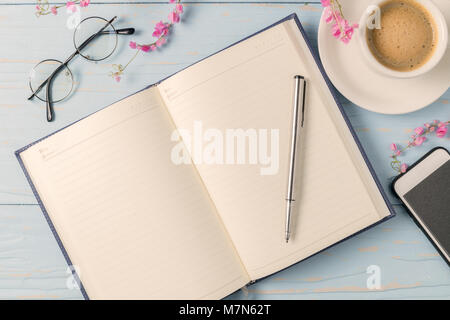 pen on blank diary book with hot black coffee and glasses on old blue wood background, vintage tone Stock Photo