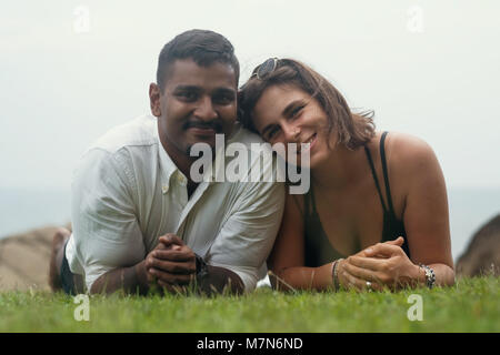 Young romantic mixed race couple lying in park on green grass. Stock Photo