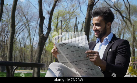 Mulatto guy reading newspaper in caf and smiles.   Stock Photo