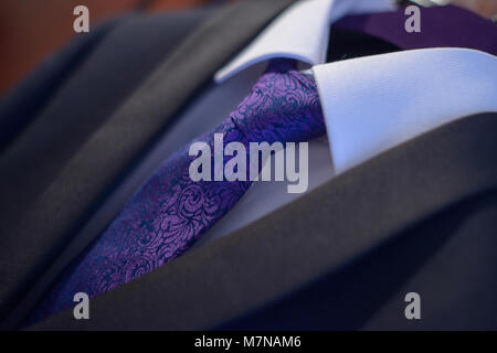 Close-up elegant suit with white shirt and purple silk necktie tied in a Windsor knot in preparation for a formal event, job interview or a wedding Stock Photo