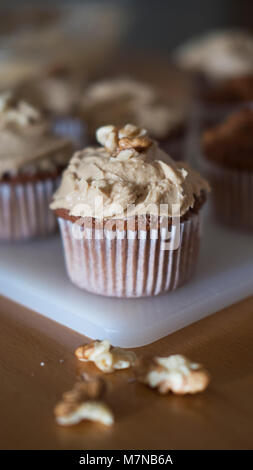 Vertical shot of coffee and walnuts homemade cupcakes with coffee icing, just taken out of the oven, positioned on a rustic white plastic board Stock Photo