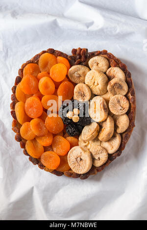 Dried fruits apricots figs prunes raisins hazelnuts on a white crumpled texture in the shape of an apple Stock Photo
