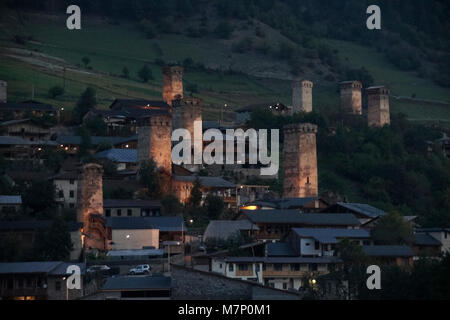 Historic tower houses lighted at night stand amid more modern homes on a hillside in Mestia, Svaneti region of the Caucasus Mountains, Georgia Stock Photo