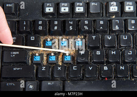 Close up filthy computer keyboard with a few keys removed, cleaning debri that has collected under keys with long cotton swab. keyboards can become cl Stock Photo