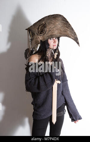 Beautiful girl dressed in witch or shaman halloween costume with black feathers and crow head on white background with shadows Stock Photo