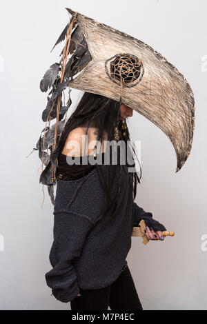 Beautiful girl dressed in witch or shaman halloween costume with black feathers and crow head on white background with shadows Stock Photo