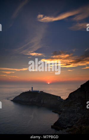 South Stack lighthouse at sunset, Anglesey, North Wales with sun shining over a calm sea Stock Photo