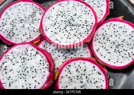 Several pieces of a sliced white pitahaya on the wet black plate. Closeup horizontal photo. Stock Photo