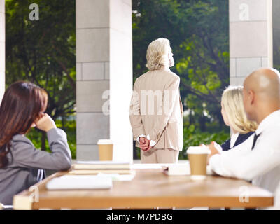 caucasian corporate business leader standing thinking during meeting, hands behind back, rear view. Stock Photo