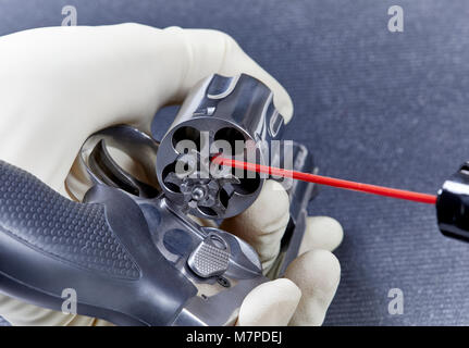 A gloved hand applying a lubricant to the ejector of a snubnose revolver isolated on a black mat Stock Photo