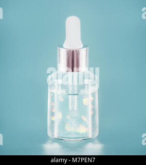 Cosmetic transparent liquid product in glass bottle with dropper. Gold Serum skin care on light blue background, front view with copy space. Beauty pr Stock Photo