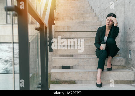 Upset business woman sitting on the stairs tired from work, sad, worried and frustrated with life.Fired from job. Stock Photo