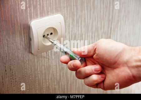 Man electrician checks the presence of electrical voltage in the socket phase. Stock Photo