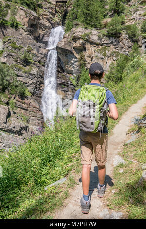 Young hiker with backpack on a mountain path, Lillaz waterfalls near Cogne, Gran Paradiso national park, Aosta Valley in the Alps, Italy