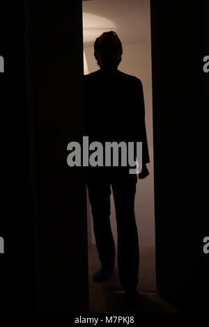 Backlit man entering a room through a door from a hallway looking threatening Stock Photo