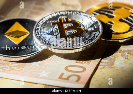 Cryptocurrency coins over euro banknotes; Bitcoin, Ethereum and Ripple coin Stock Photo