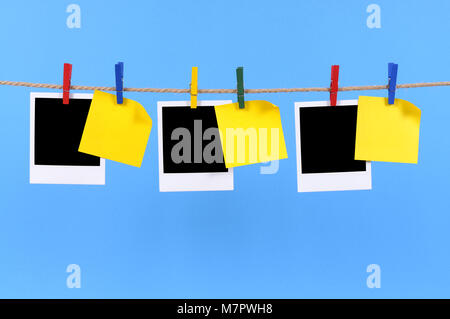 Blank instant camera photo prints and office sticky notes hanging on a rope or string isolated against a blue background.  Space for copy. Stock Photo