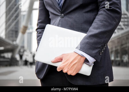 Smart businessman wear suit hold laptop, computer, to office for his working business conference in downtown with office in high skyline building Stock Photo