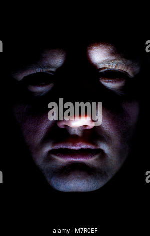 Close-up portrait of young Caucasian Ethnicity man's face illuminated from below with flashlight on black background Stock Photo