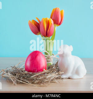 Red egg in the nest and rabbit beside them on wooden board. Easter composition. Close up. Stock Photo