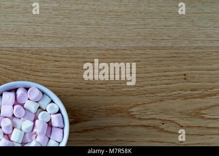 Lay flat view of mini marshmallows in white cup on oak surface Stock Photo