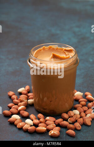 peanut butter in a glass jar, peanuts on a gray concrete background. Stock Photo