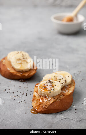 healthy breakfast. sandwich with peanut butter, banana, honey, chia seeds and coconut sprinkled on a gray concrete background Stock Photo