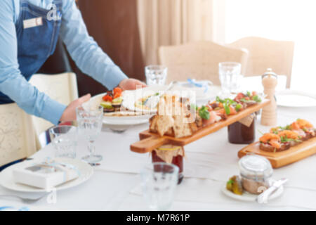 Blurred background. Waiter serving meat dishes on wooden board at restaurant, close up view. Stock Photo